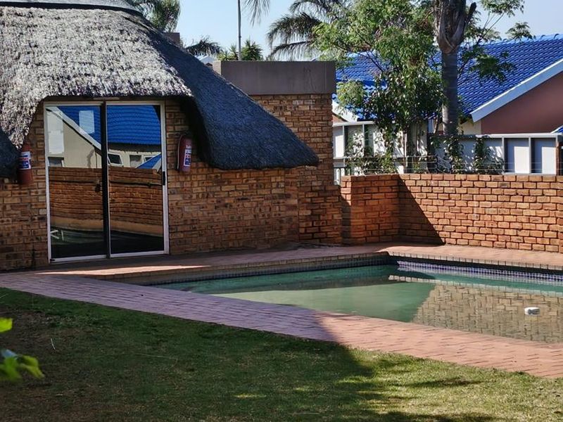 Outdoor pool area featuring a swimming pool with paved surround, brick boundary walls, and a structure with a traditional thatch roof.