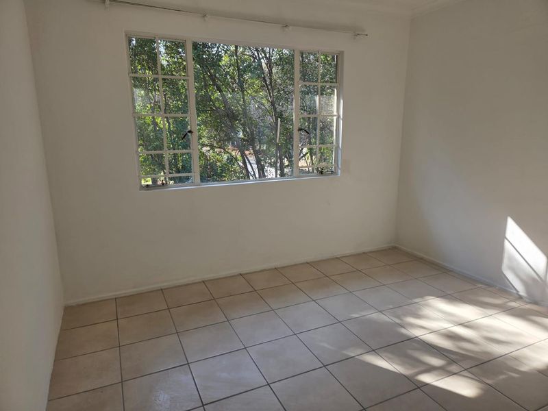 An empty bedroom featuring neutral tiled flooring and a large grid-pattern window providing natural light and a view of the surrounding trees.