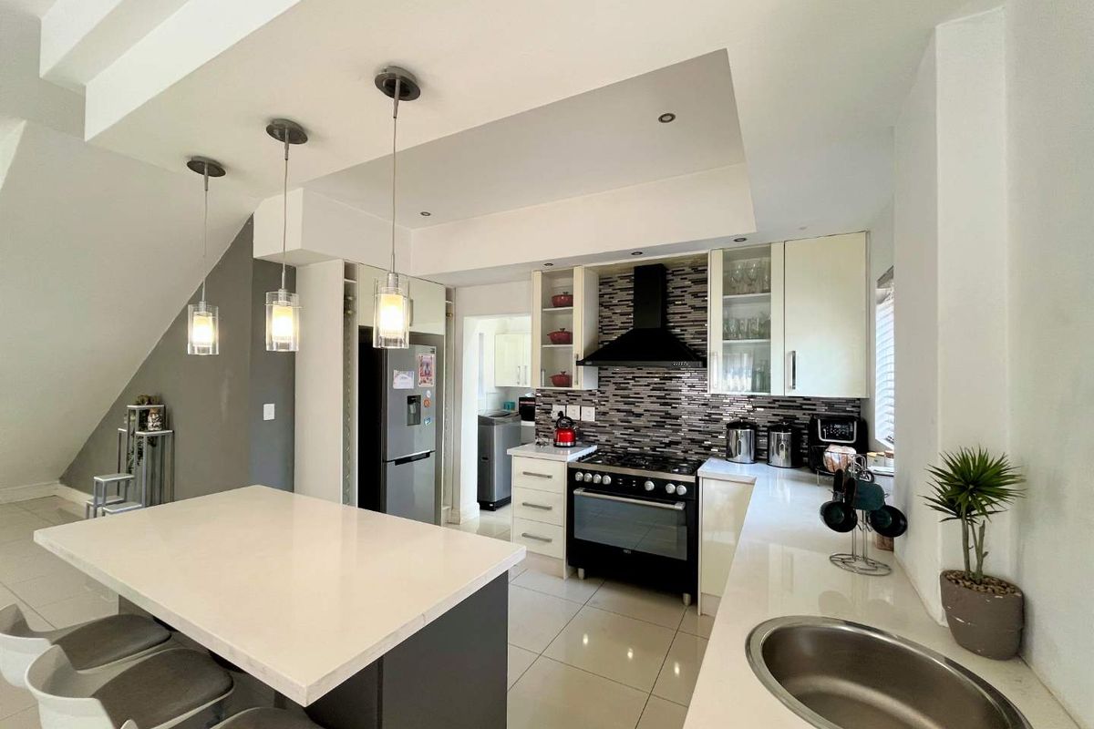 Modern kitchen featuring a central island with stone countertops, built-in oven, extractor fan, and stylish pendant lighting, offering a functional and contemporary cooking space.