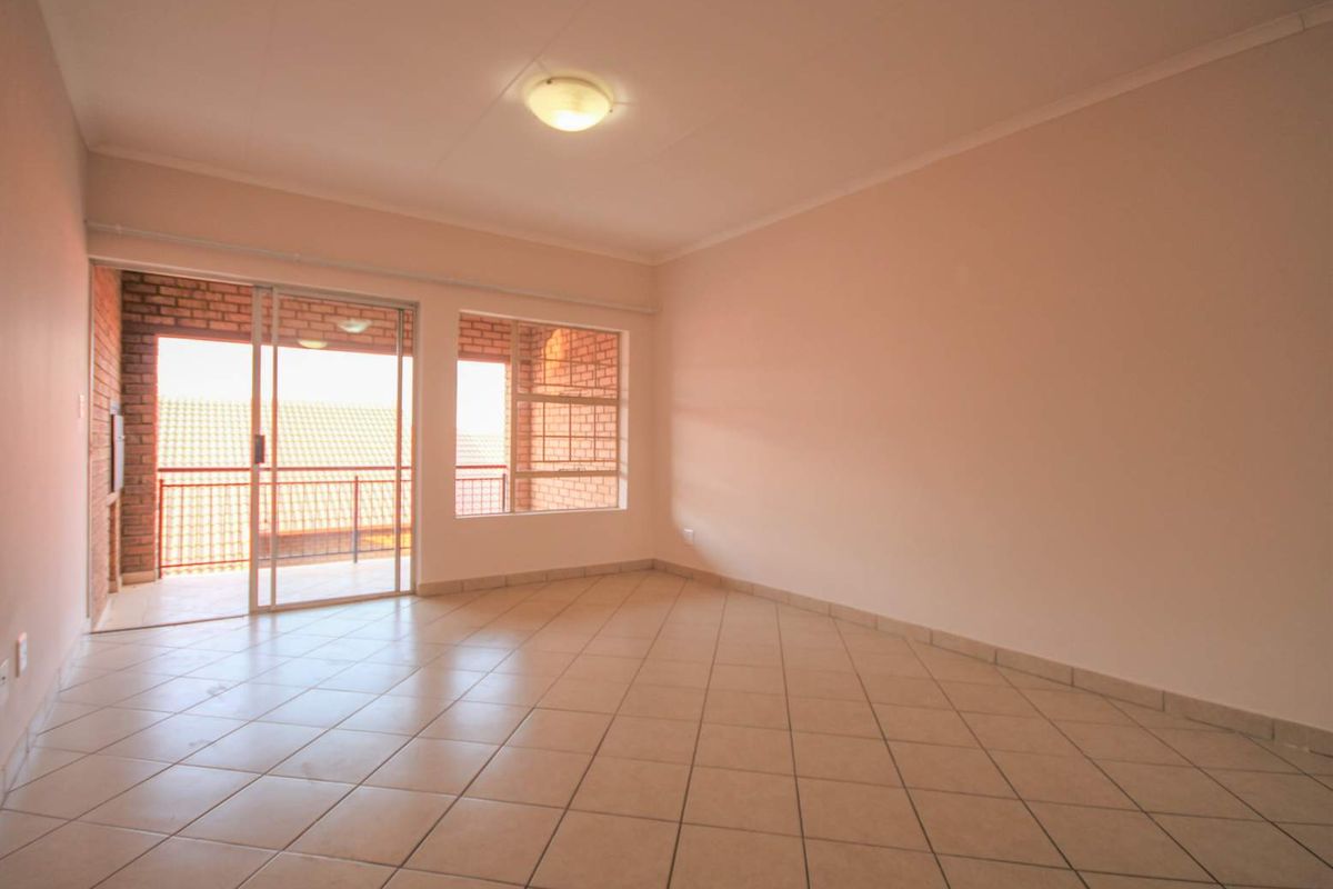 A bright, empty living room featuring tiled flooring and a sliding glass door that opens onto a private balcony.
