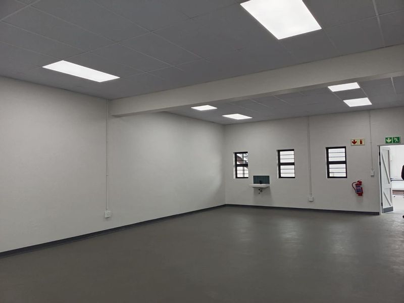 A clean, open-plan industrial utility space featuring a suspended ceiling, recessed lighting, durable concrete flooring, and a wall-mounted basin.