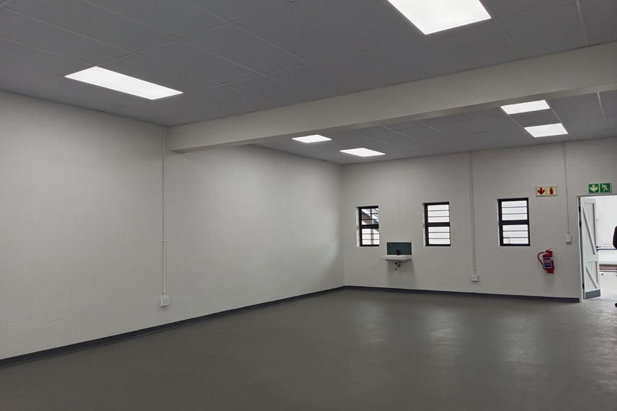 A clean, open-plan industrial utility space featuring a suspended ceiling, recessed lighting, durable concrete flooring, and a wall-mounted basin.