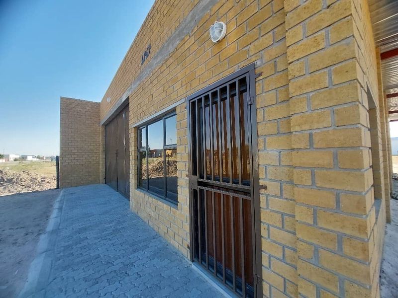 Exterior view of an industrial property featuring a face brick facade, secure entrance gate, aluminium windows, and a paved driveway area.