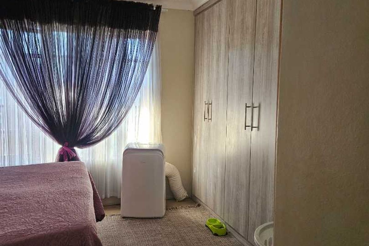 A bedroom featuring built-in wooden cabinetry and a large window with curtaining.