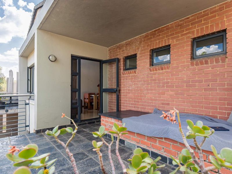 A covered balcony featuring slate tile flooring, an exposed brick wall, and a built-in brick bench, offering a functional outdoor living space.