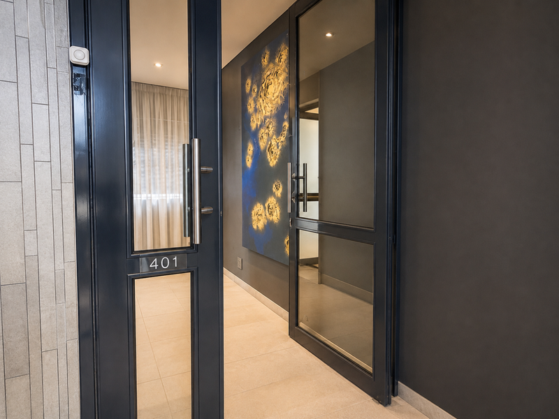 Modern penthouse entrance featuring sleek glass-panelled double doors, contemporary tiled flooring, and sophisticated dark wall finishes with recessed lighting.