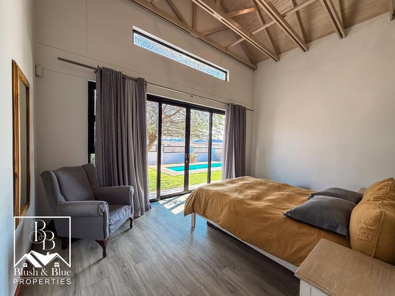 Spacious bedroom featuring a vaulted timber ceiling, laminate flooring, and sliding glass doors providing direct access to the pool area.