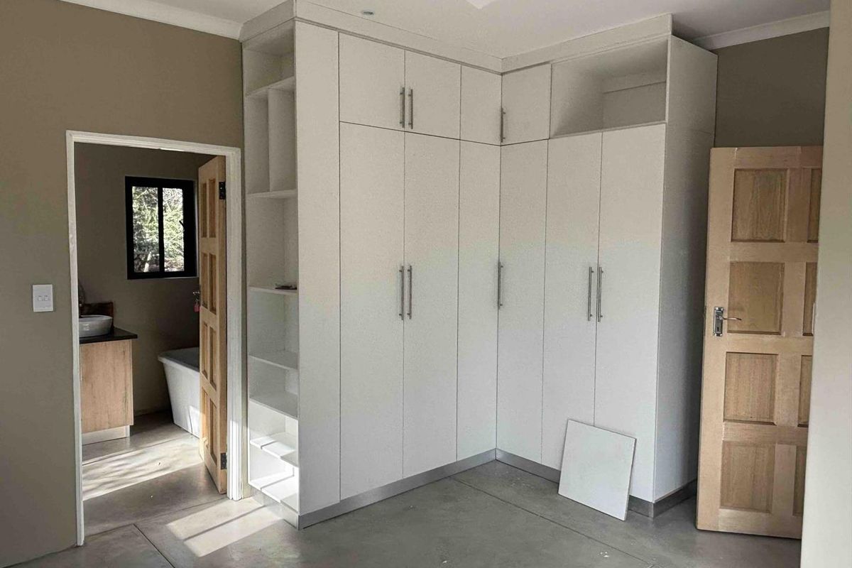 A bedroom featuring built-in white cupboards, polished concrete flooring, and direct access to an en-suite bathroom.