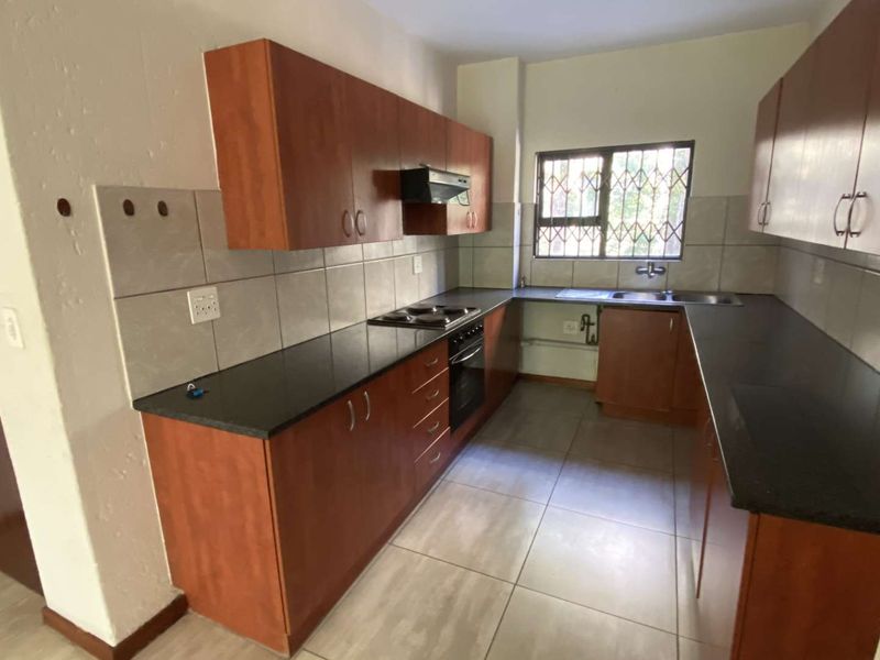 A functional kitchen featuring wood-finish cabinetry, dark countertops, built-in oven and hob, tiled backsplash, and tiled flooring.