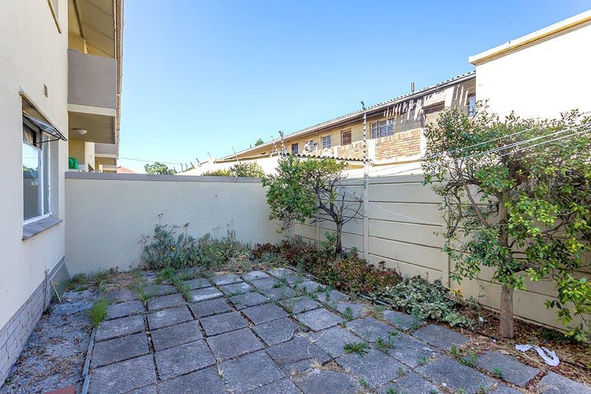 A private rear courtyard area featuring paved flooring, a boundary wall with electric fencing, and established garden beds.