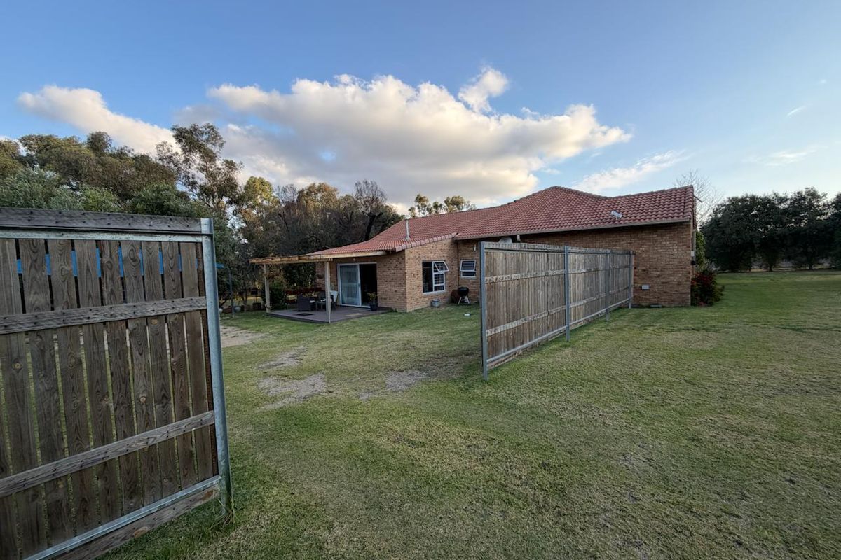 Rear view of a brick cottage featuring a tiled roof, a timber deck, and surrounding garden space with timber fencing.