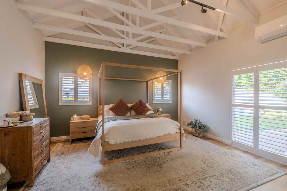 Spacious bedroom featuring vaulted exposed beam ceilings, plantation shutters, and a split-system air conditioning unit.