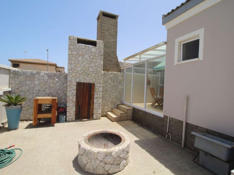 Outdoor patio area featuring a stone-clad fireplace, a matching stone fire pit, and a glass-enclosed section, perfect for entertaining.