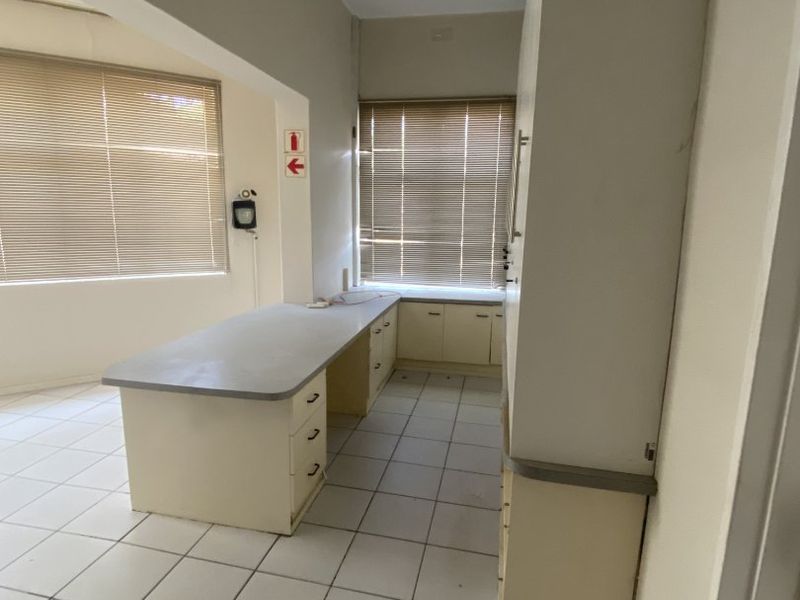 A functional office space featuring built-in cabinetry, laminate work surfaces, ceramic tile flooring, and large windows with venetian blinds.