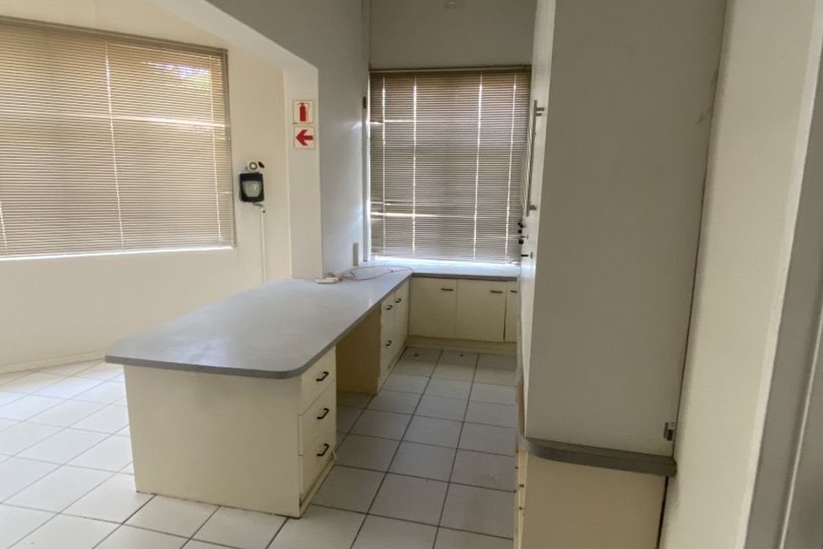 A functional office space featuring built-in cabinetry, laminate work surfaces, ceramic tile flooring, and large windows with venetian blinds.
