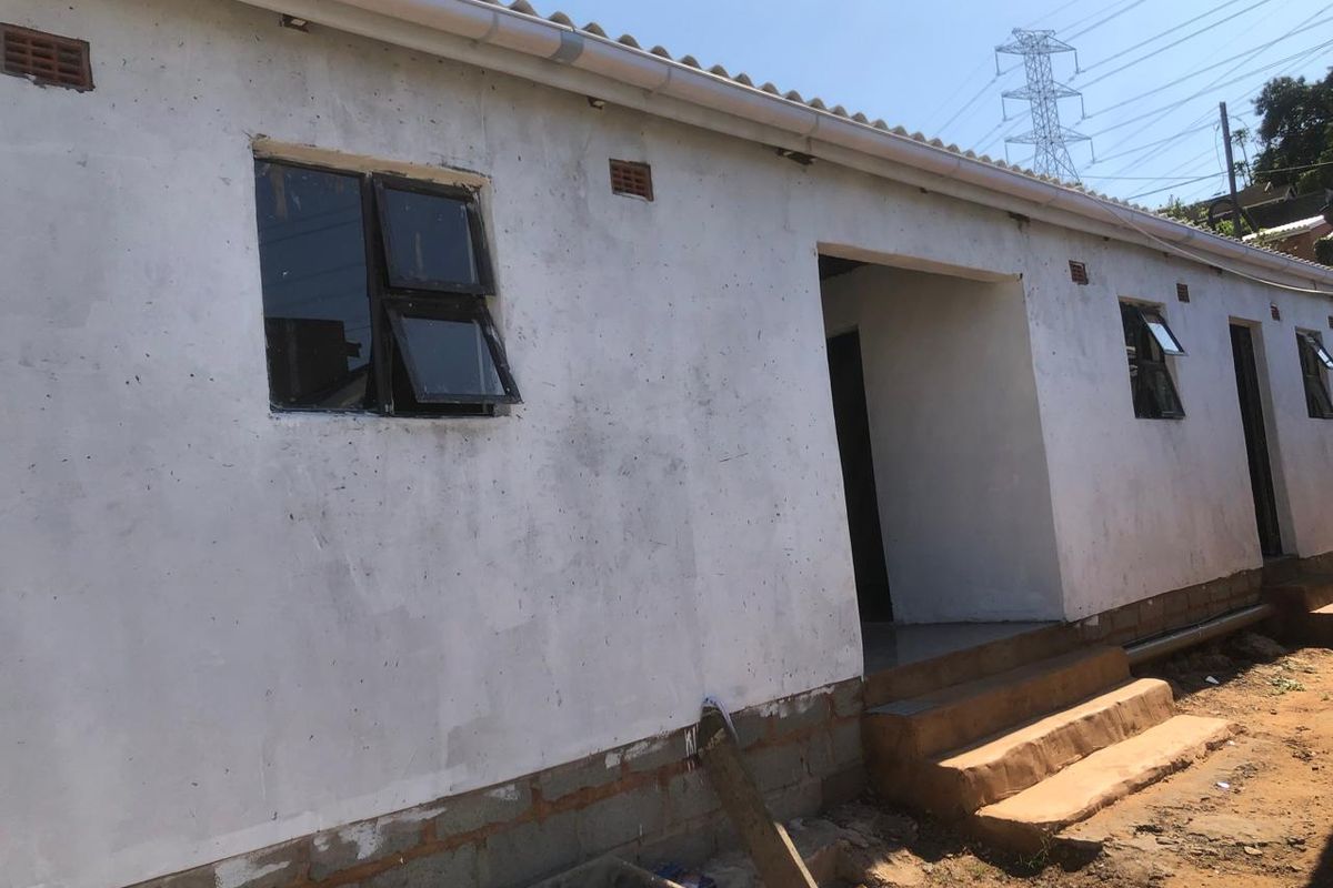 Rear exterior view of a cottage featuring unfinished plaster walls, concrete steps, and aluminium window frames, requiring further maintenance and finishing work.