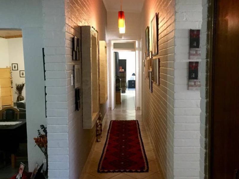 A well-lit interior hallway featuring white painted brick walls, tiled flooring, and a central pendant light fixture leading through the home.