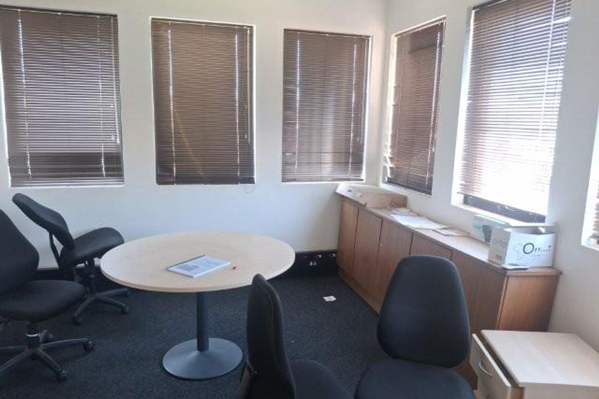 A functional office space featuring multiple windows with venetian blinds, built-in storage cabinetry, and dark carpeting.