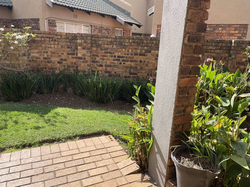 A private rear garden featuring a paved patio area, established garden beds, and a brick boundary wall.