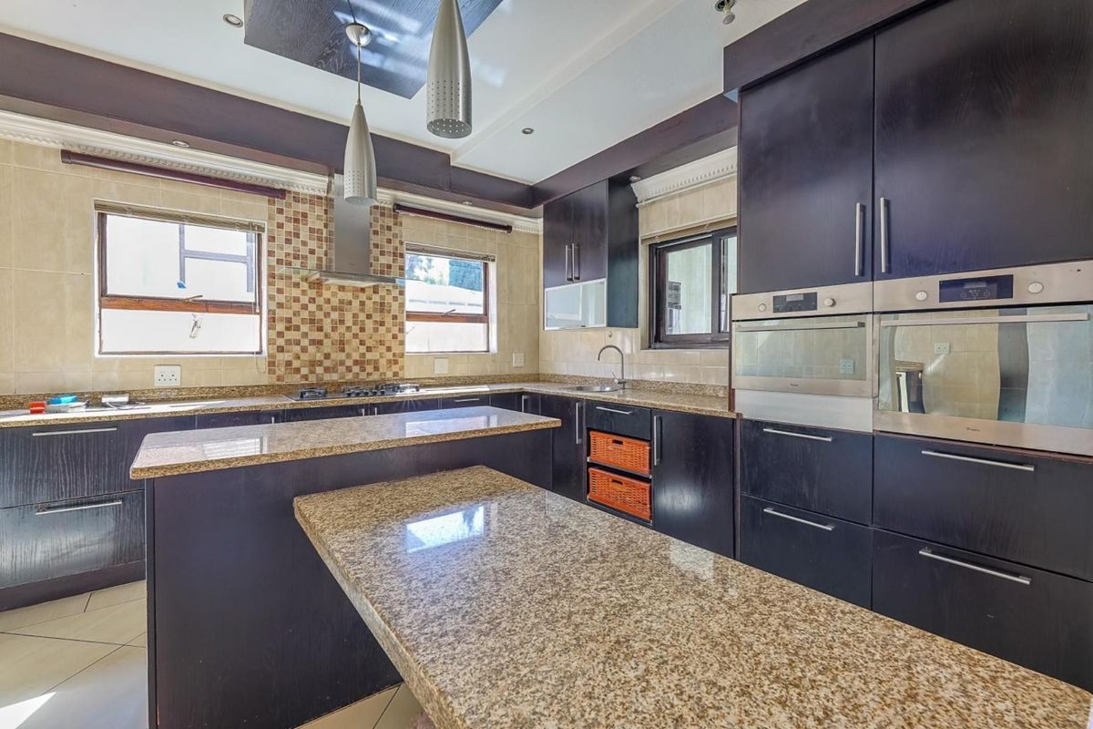 Modern kitchen featuring dark wood cabinetry, granite countertops, a central island, and built-in stainless steel appliances including dual ovens and a gas hob.