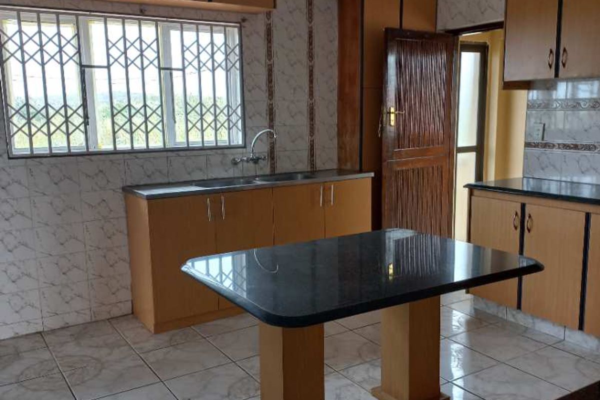 A functional kitchen featuring wooden cabinetry, granite countertops, a central island, and tiled flooring with security bars on the window.