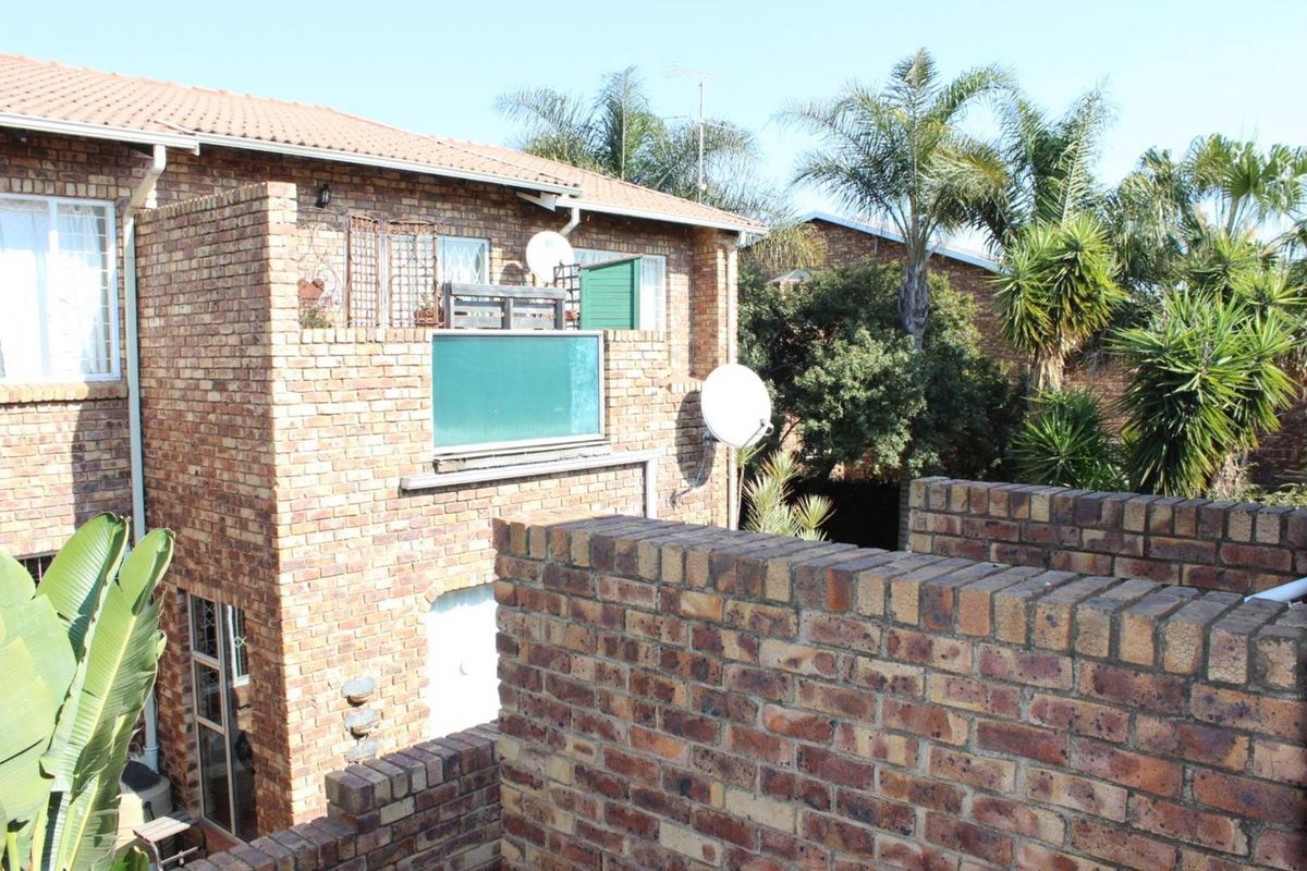 Exterior view of a face-brick townhouse featuring a balcony with a privacy screen and established garden surroundings.