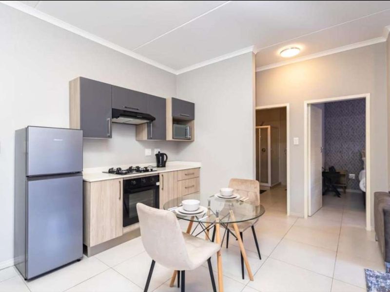 Modern open-plan kitchen featuring sleek two-tone cabinetry, integrated appliances, and tiled flooring, seamlessly flowing into the adjacent living and bedroom areas.