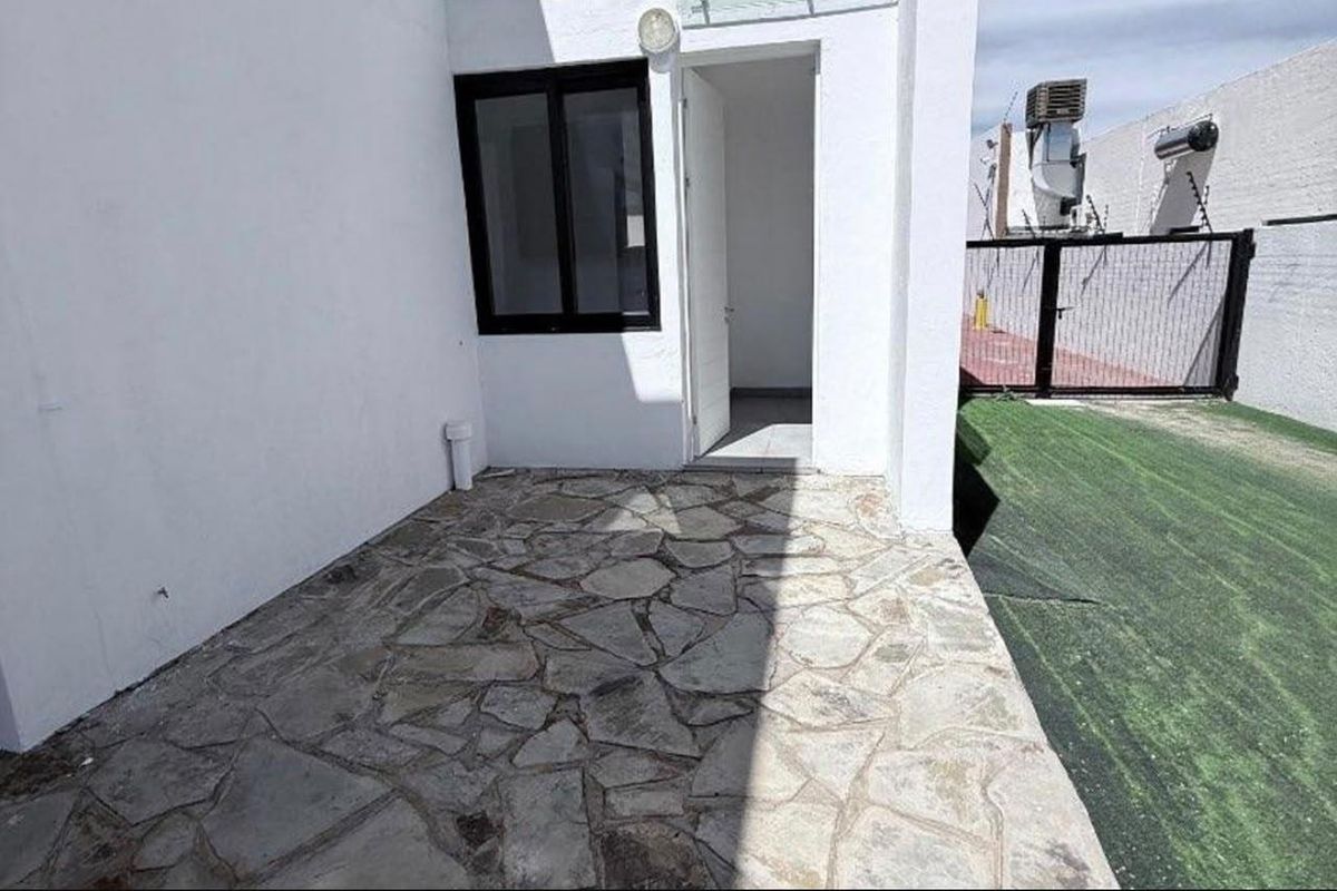 A private outdoor patio area featuring flagstone paving, adjacent to a small artificial turf garden and secured by a metal gate.