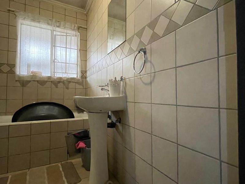 A dated bathroom featuring a pedestal basin, bathtub, and full-height ceramic wall tiling. The space would benefit from modern updates to finishes and fixtures.