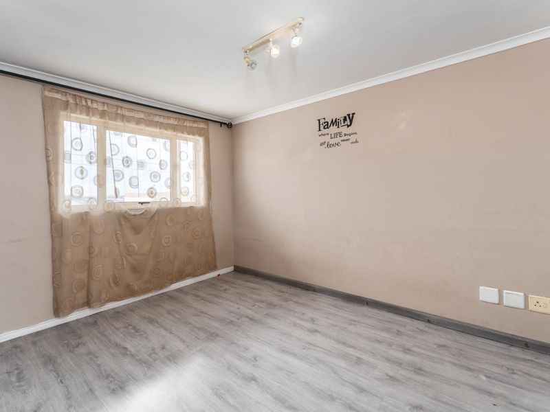 A vacant bedroom featuring grey laminate flooring, neutral walls, and a ceiling-mounted spotlight fixture, offering a blank canvas for personalization.