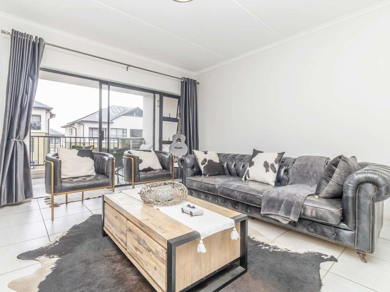 A bright and spacious living room featuring large sliding glass doors that open onto a balcony, with neutral tiled flooring throughout.