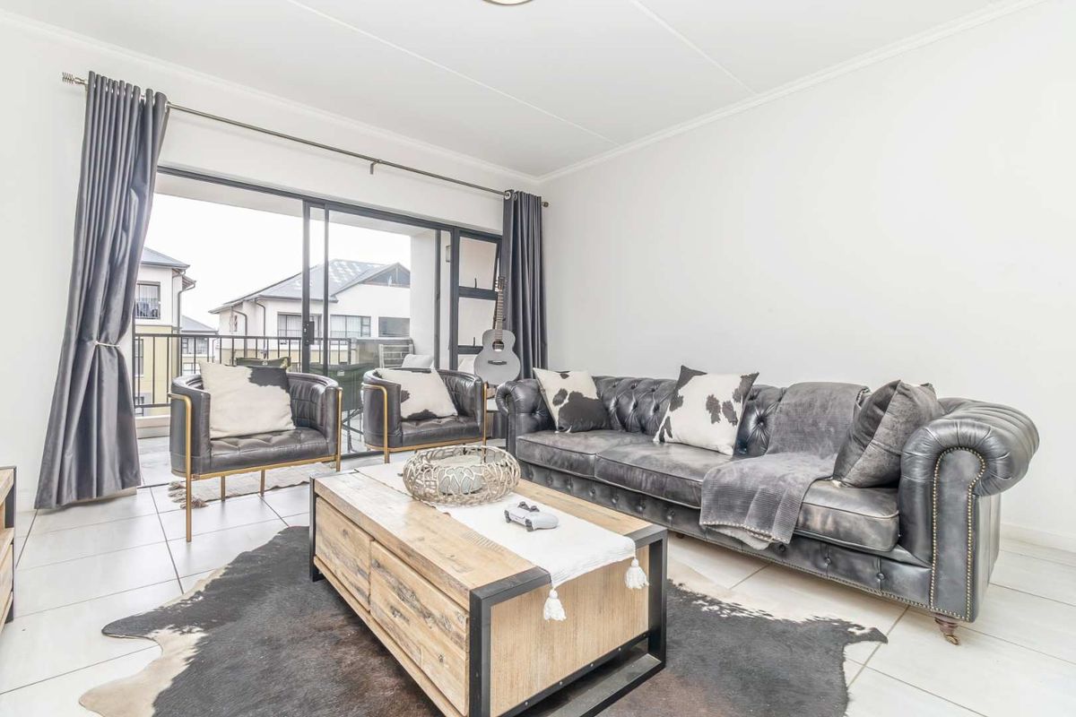 A bright and spacious living room featuring large sliding glass doors that open onto a balcony, with neutral tiled flooring throughout.