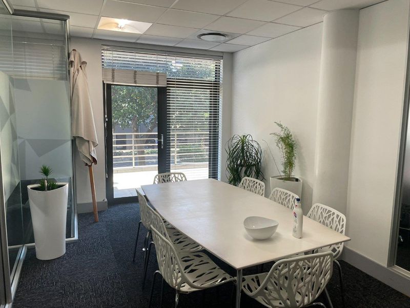 A professional office meeting room featuring carpeted flooring, a suspended ceiling with recessed lighting, and a glass partition with access to an outdoor area.