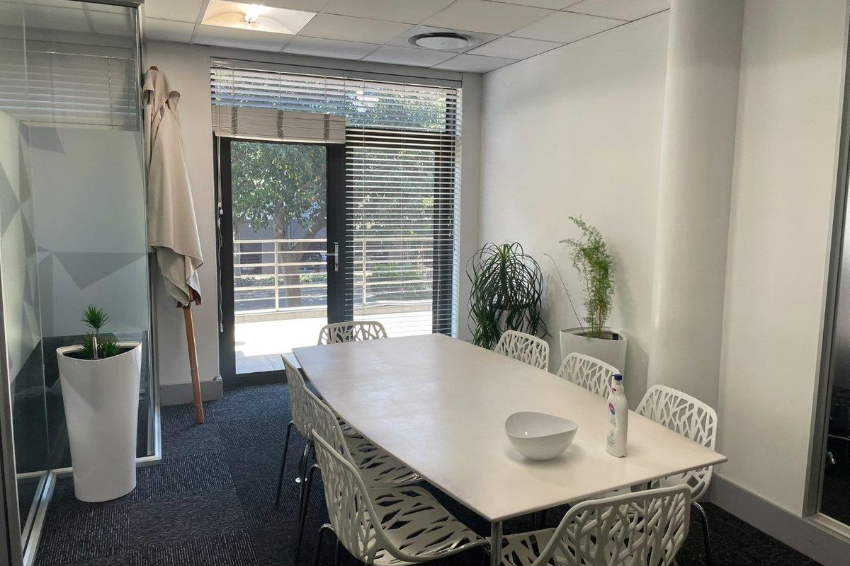 A professional office meeting room featuring carpeted flooring, a suspended ceiling with recessed lighting, and a glass partition with access to an outdoor area.