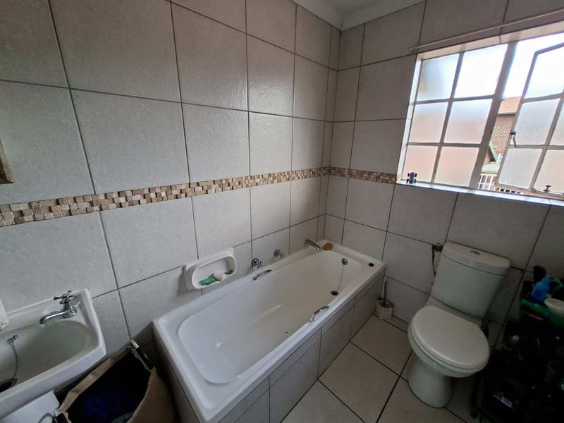A functional bathroom featuring a built-in bathtub, wall-mounted basin, and toilet, finished with neutral ceramic wall and floor tiles.