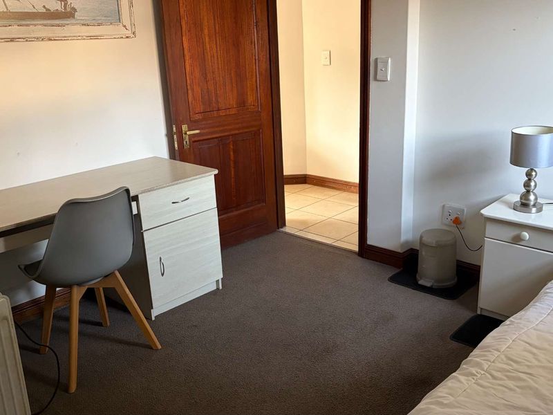 A functional bedroom featuring carpeted flooring, a timber door, and access to an adjacent tiled room.
