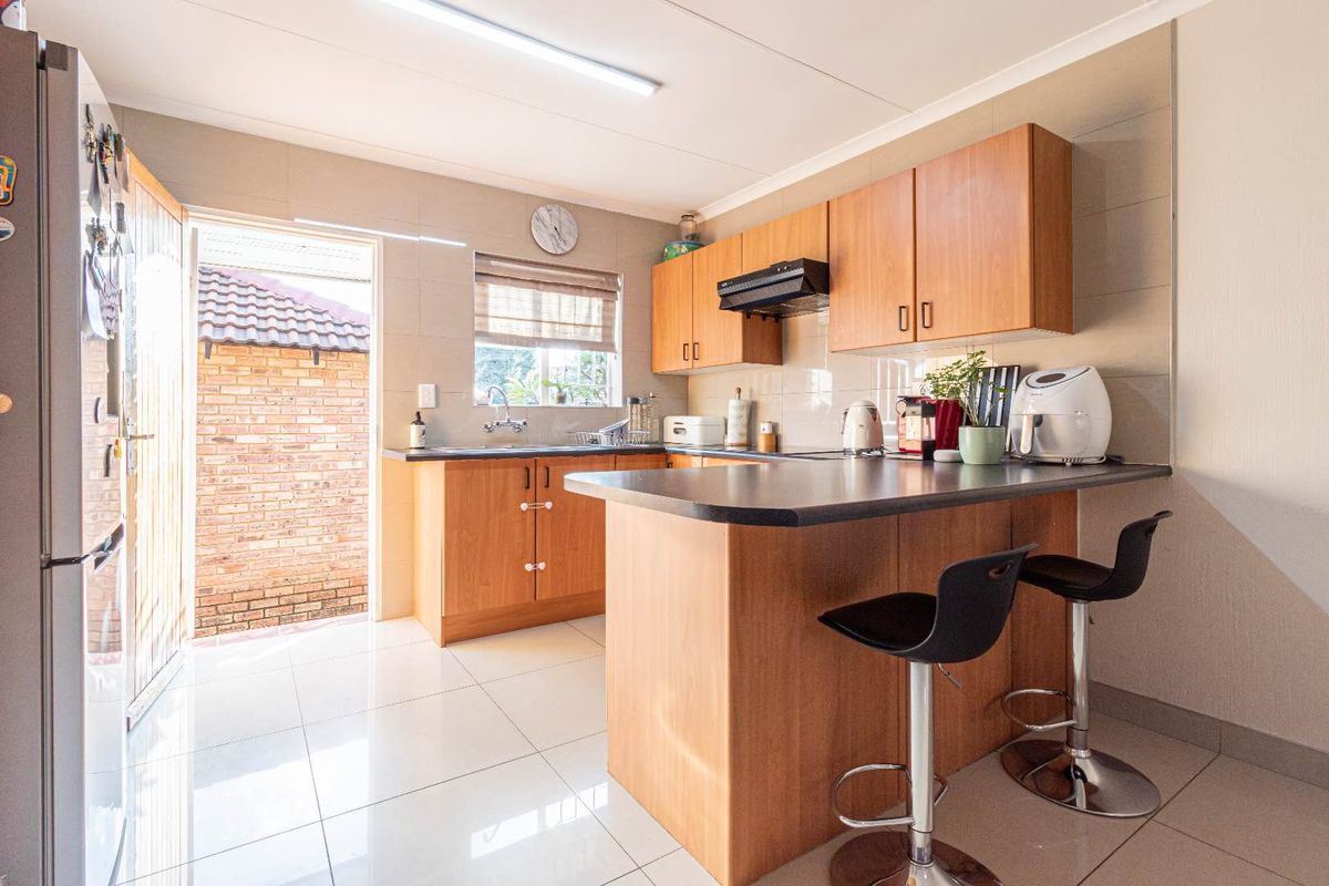 Functional kitchen featuring wood-finish cabinetry, dark laminate countertops, tiled flooring, and a breakfast bar, with direct access to the exterior.