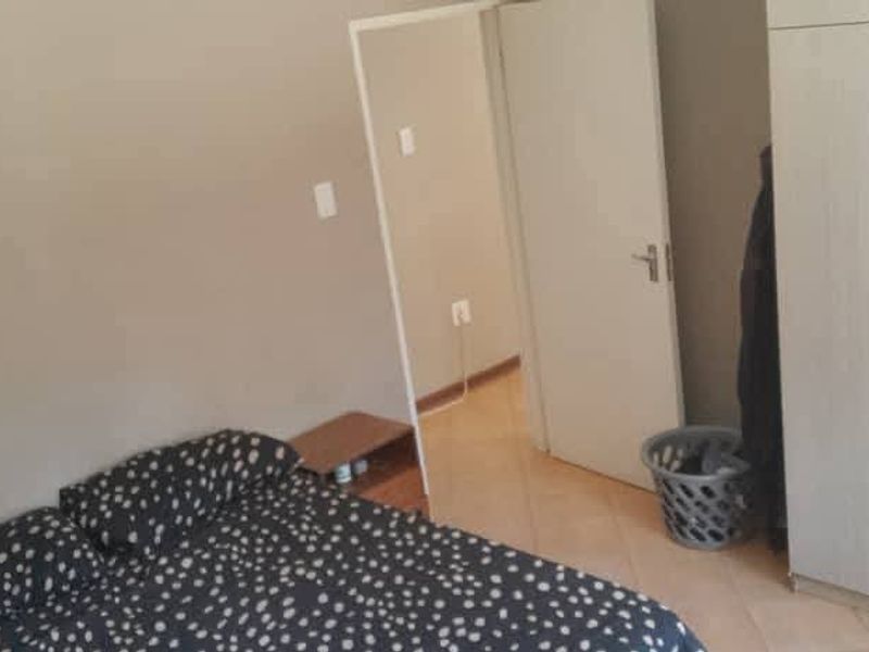 A bedroom featuring tiled flooring and a built-in wardrobe, with an adjacent doorway leading to another area of the apartment.