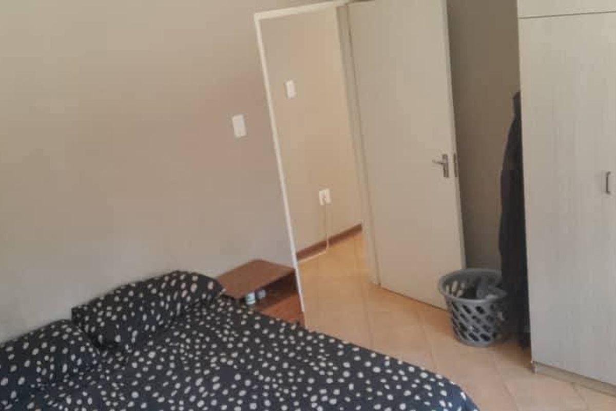 A bedroom featuring tiled flooring and a built-in wardrobe, with an adjacent doorway leading to another area of the apartment.