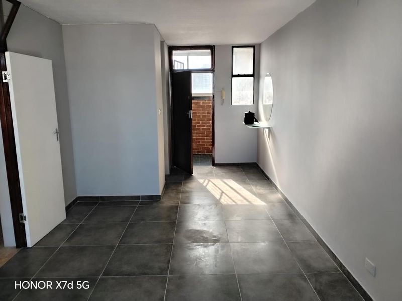 A clean, empty entrance area featuring neutral grey walls and dark tiled flooring, leading to an exterior doorway.