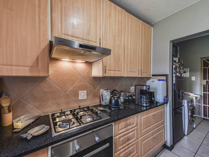 Functional kitchen featuring light wood cabinetry, granite countertops, a gas hob, built-in oven, and a tiled backsplash, with an adjacent laundry area.