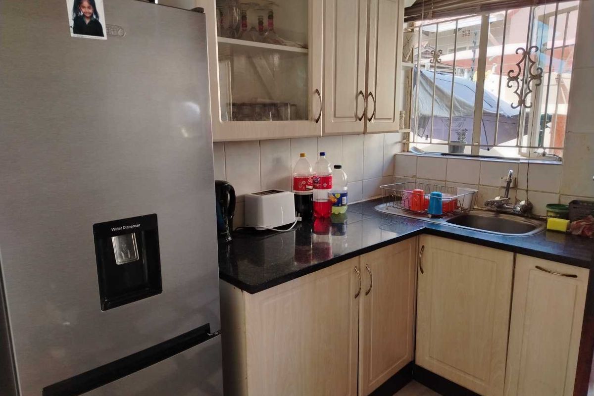 A compact kitchen featuring light-toned cabinetry, dark granite countertops, a stainless steel sink, and a window with security bars.
