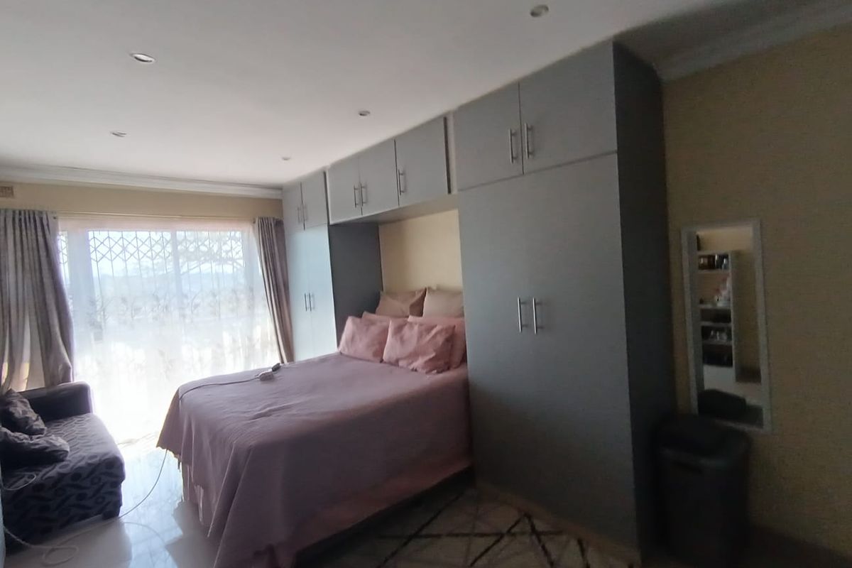 A well-lit bedroom featuring extensive built-in cabinetry, tiled flooring, and a large window with security gate access.