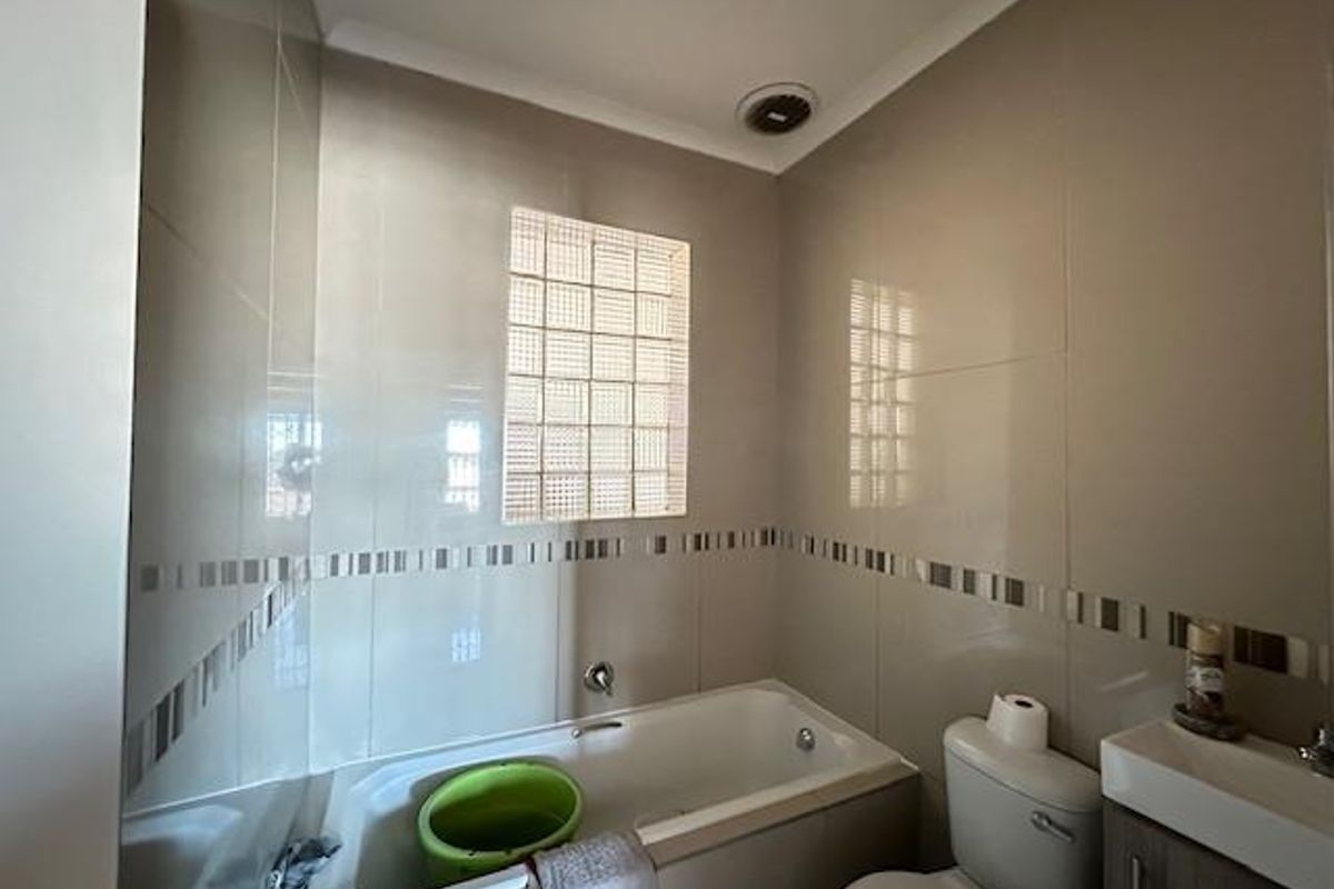 A compact bathroom featuring full-height wall tiling, a built-in bathtub, a glass block window, a toilet, and a vanity basin.