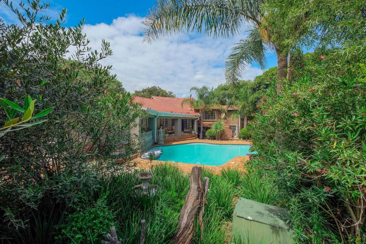 A view of the rear exterior of the house featuring a swimming pool, paved patio area, and established garden surroundings.