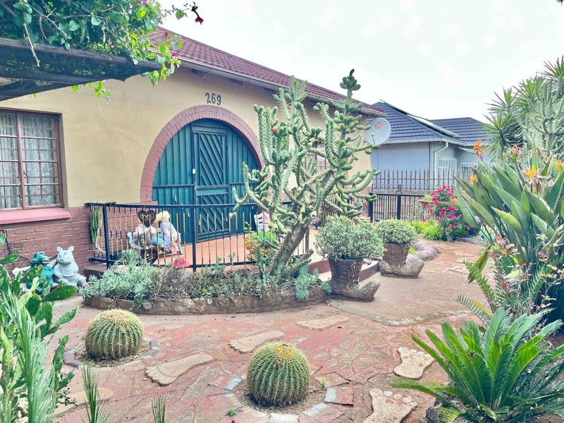 Front exterior view of a house featuring an arched entrance, security gate, and a landscaped garden with paved pathways and established plantings.
