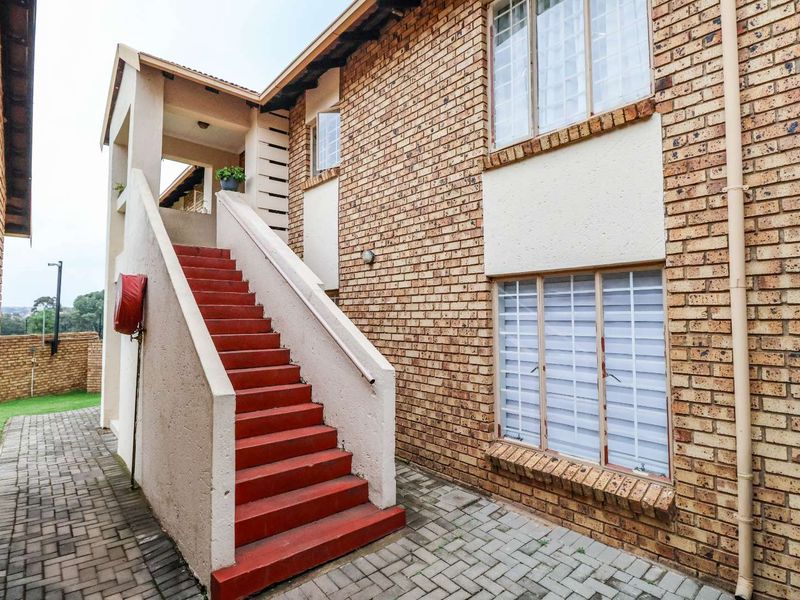 Exterior view of an apartment building featuring a brick facade, paved walkway, and an external concrete staircase with a fire hose reel.