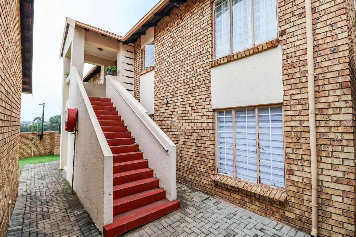 Exterior view of an apartment building featuring a brick facade, paved walkway, and an external concrete staircase with a fire hose reel.
