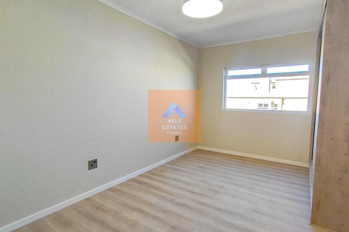 A clean, empty bedroom featuring light wood-look flooring, neutral walls, and a built-in wardrobe.