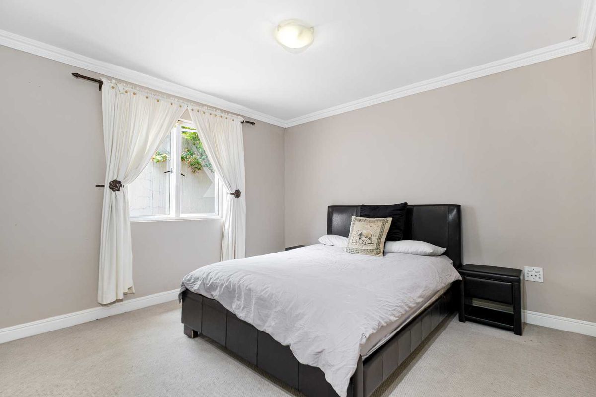 A neutrally painted bedroom featuring carpeted flooring, crown molding, and a window with curtain rods.